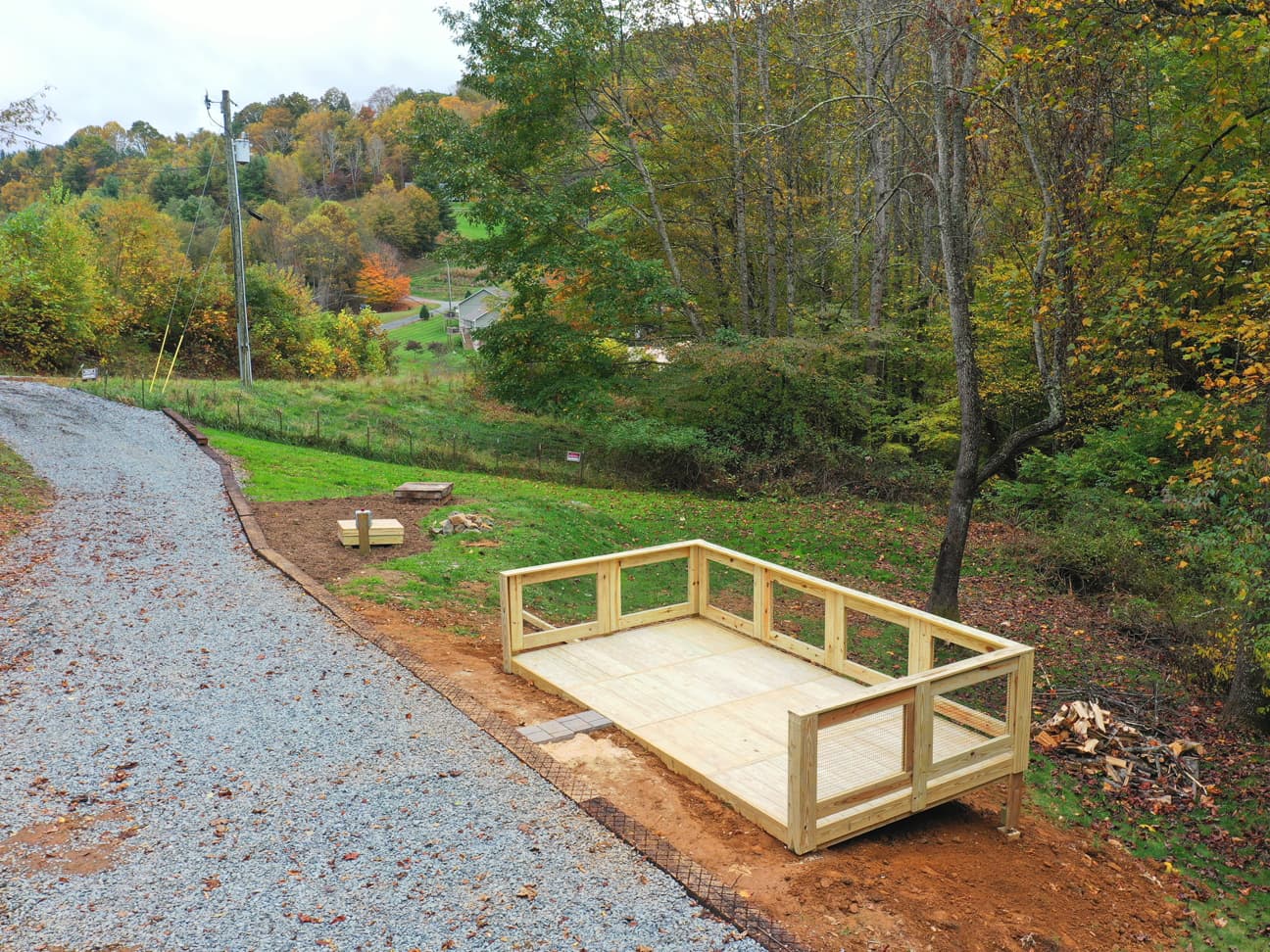 Ariel view of the deck under construction along a gravel driveway, with fall foliage covering the surrounding hillside