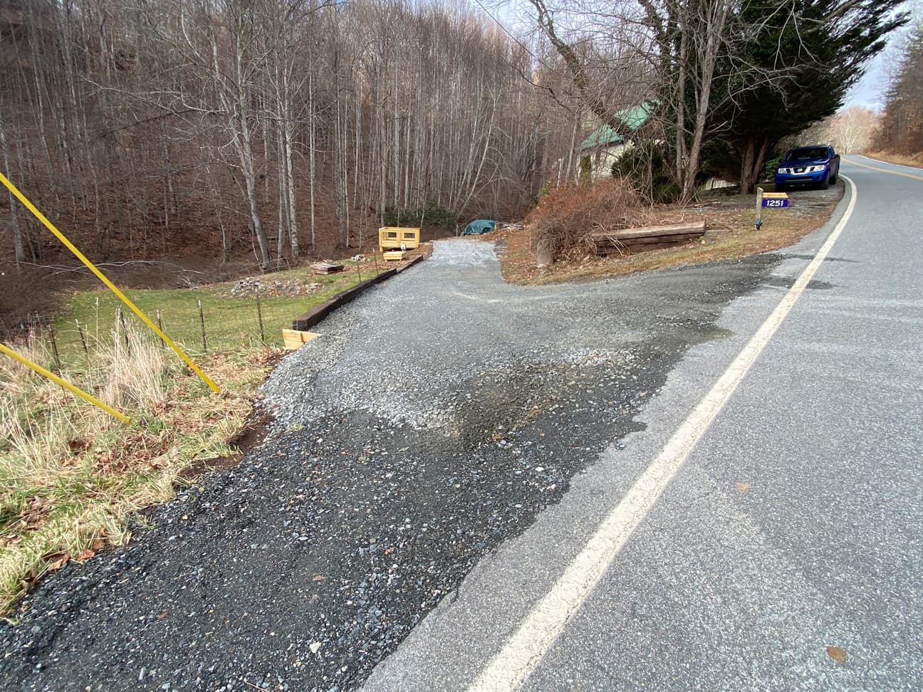 Driveway entrance from the main road, maked by the property mailbox, with the wooded site visible beyond