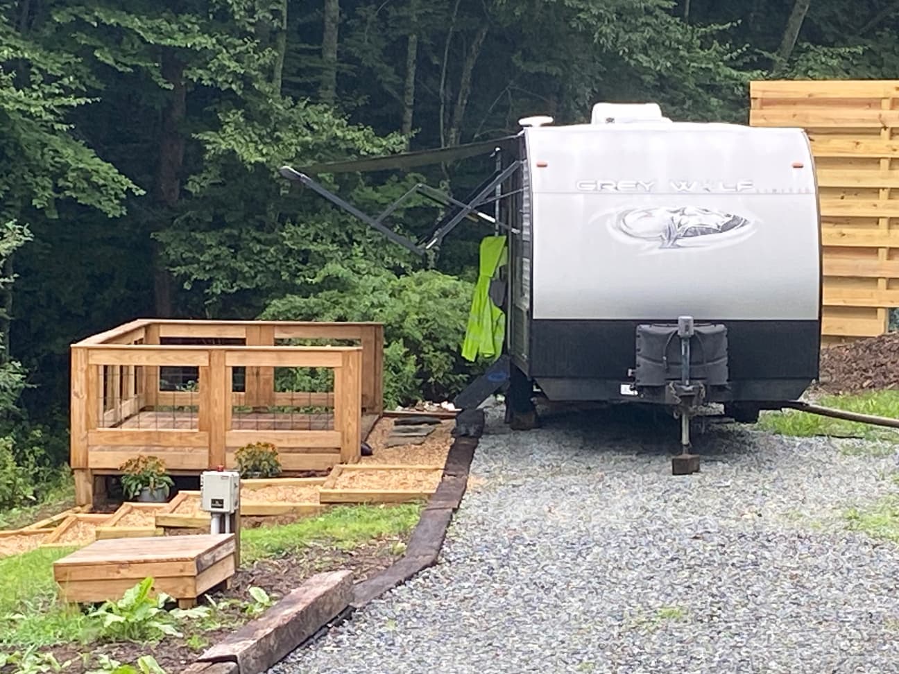 Close-up of a travel trailer with its awning extended, parked next to the finished guest deck and privacy fence panel